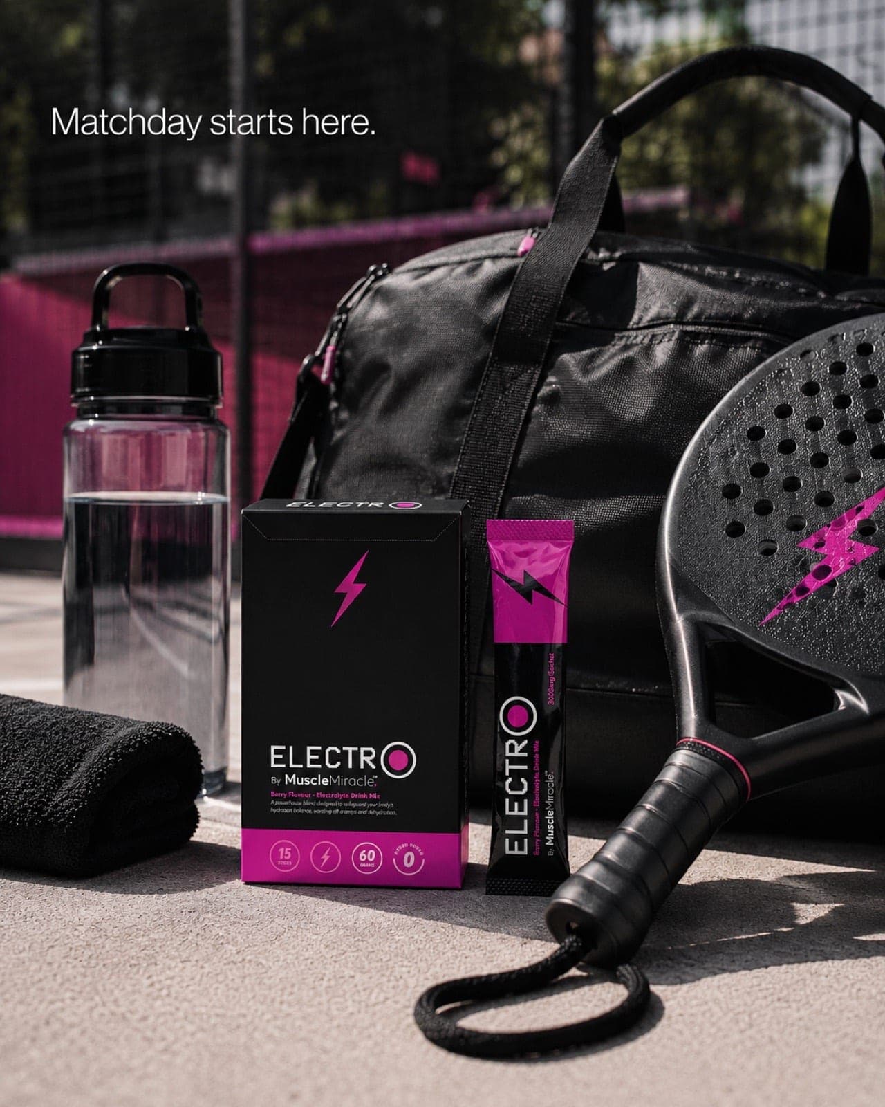 Muscle Miracle Electrolytes Berry pack and sachet beside a padel racket, kit bag and towel on court