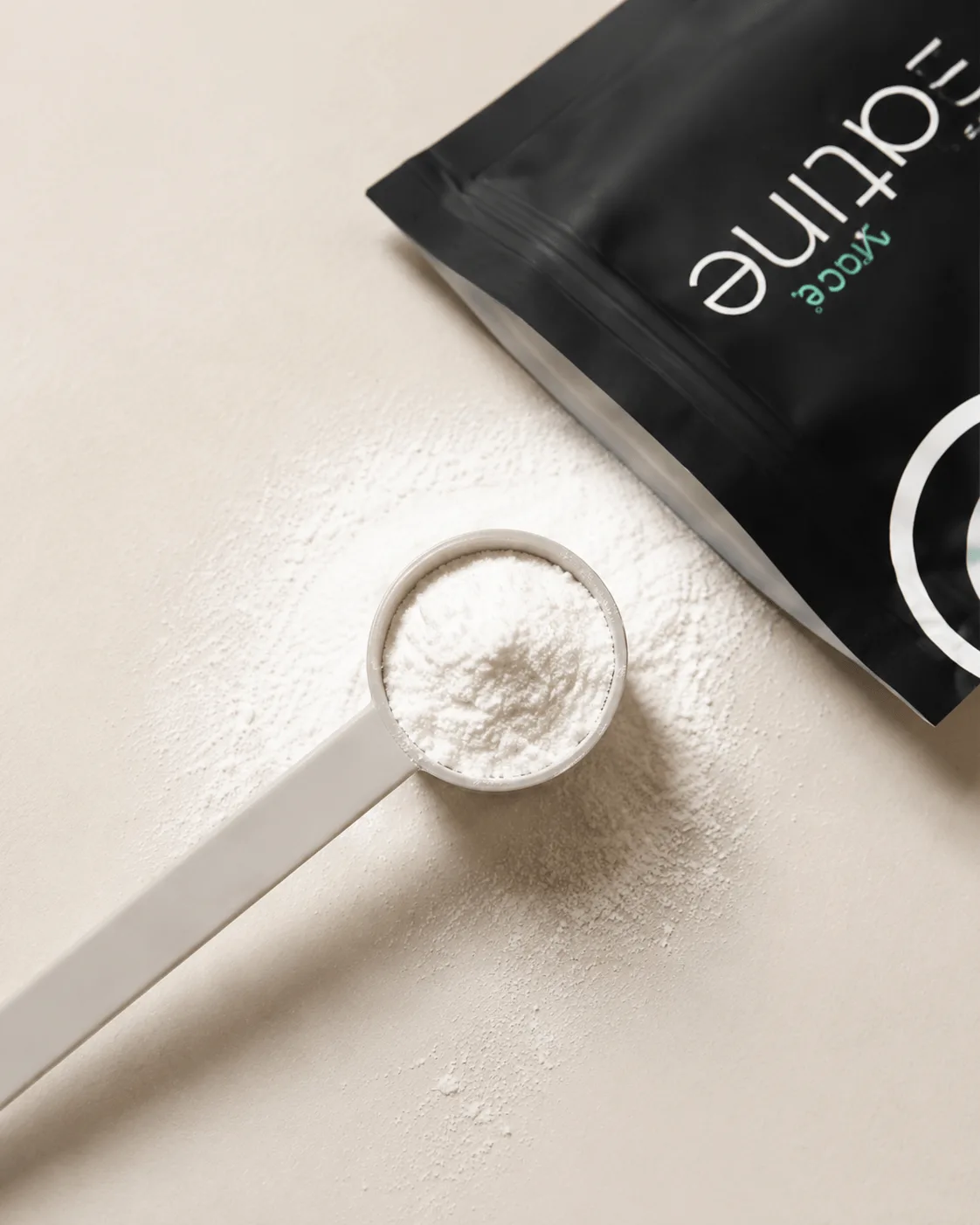 A scoop of micronised creatine powder beside the pouch on beige