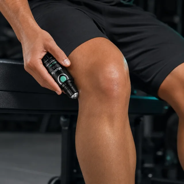 Rolling the Pain Relief Roll-On over a knee on a gym bench